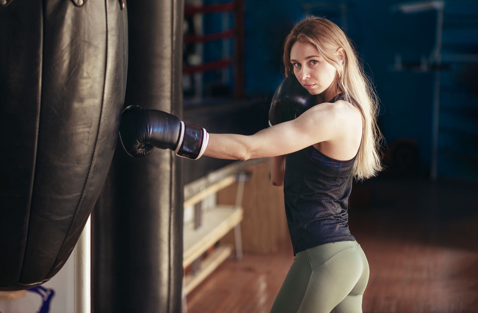 Young woman training punch boxing gloves for punching bag. Girl making Strong kick. CrossFit.